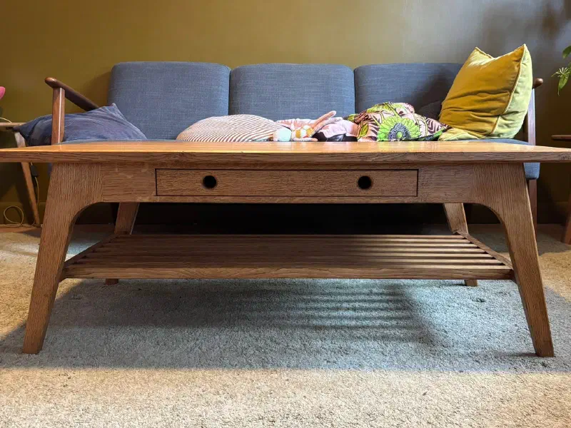 Table basse en chêne massif avec un tiroir en façade, vue de face devant un canapé bleu