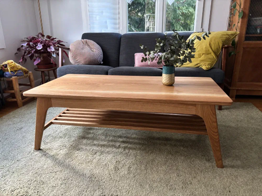 Table basse en chêne massif de trois quarts devant un canapé gris, un vase d'eucalyptus sur le plateau aux angles arrondis