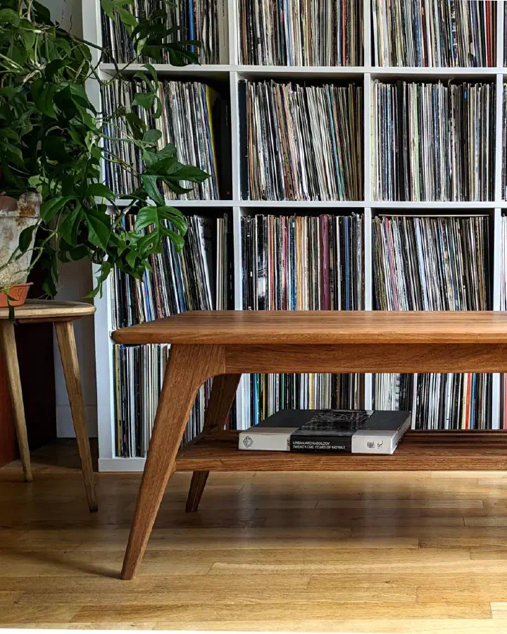 Table basse en noyer massif devant une bibliothèque de vinyles, un livre posé sur la tablette à claire-voie