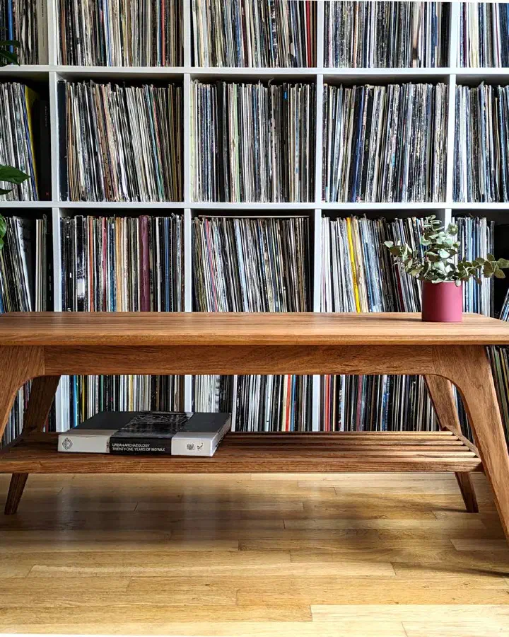 Table basse en noyer massif devant une bibliothèque de vinyles, un livre posé sur la tablette à claire-voie