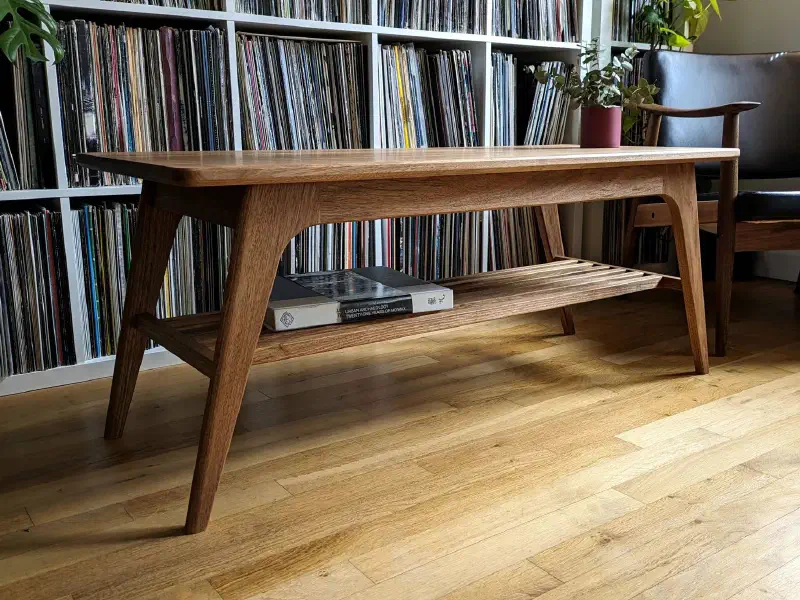 Table basse en noyer vue de trois quarts, à côté d'un fauteuil en cuir noir