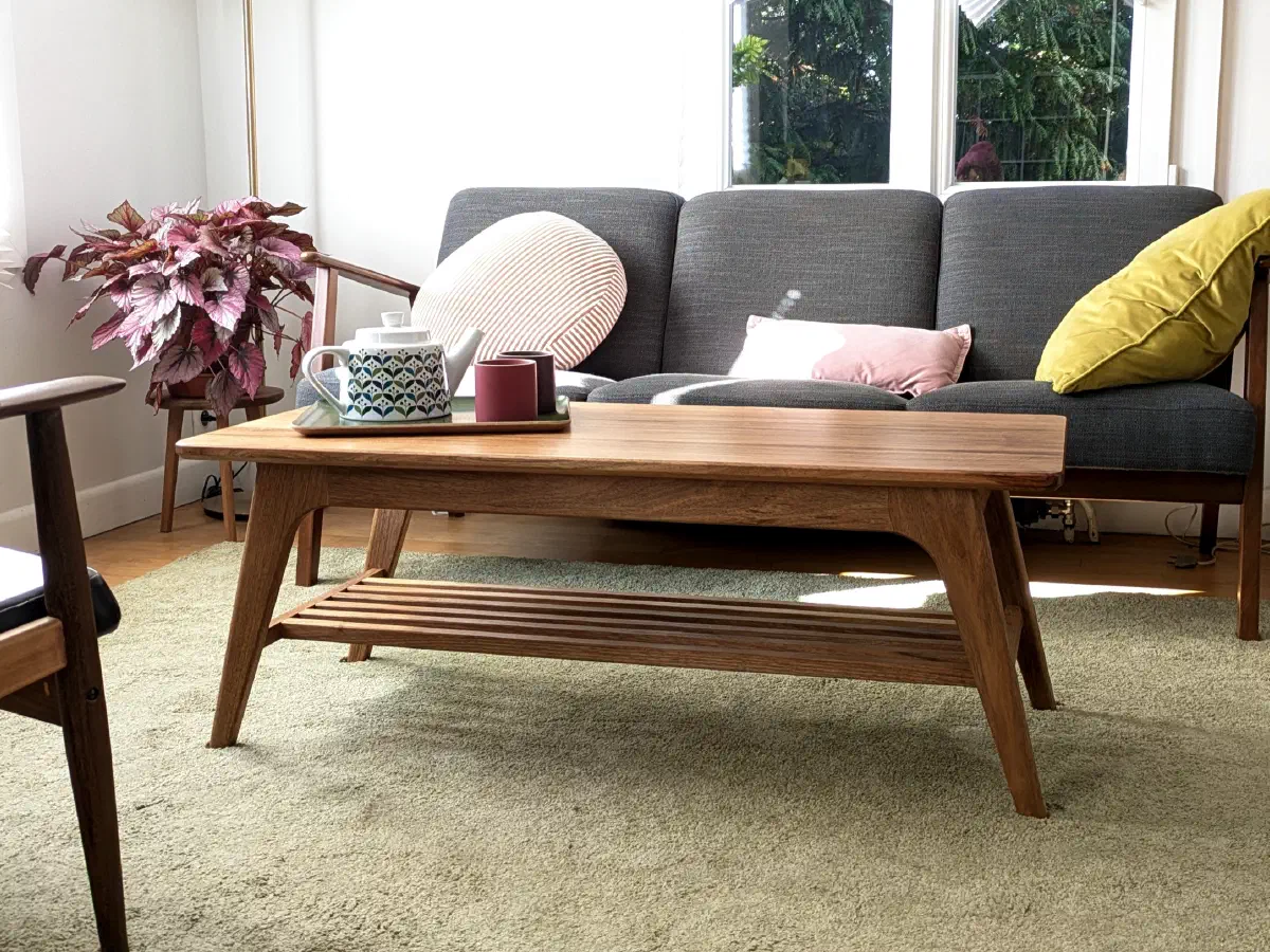 Table basse en noyer de trois quarts dans un salon lumineux, devant un canapé gris, un plateau à thé posé dessus