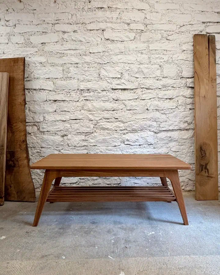Table basse en bois massif à l'atelier, devant un mur de pierres blanches et des plateaux de bois brut