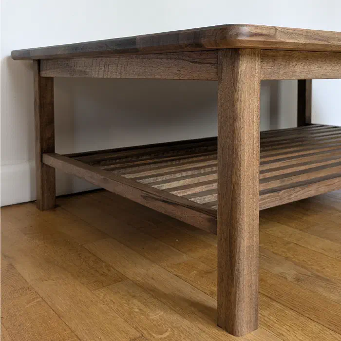 Pied droit et tablette à claire-voie de la table en noyer, vus de trois quarts au ras du parquet