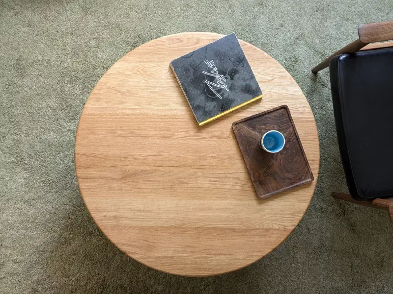 Table ronde en chêne vue du dessus, sur un tapis vert, à côté d'un fauteuil