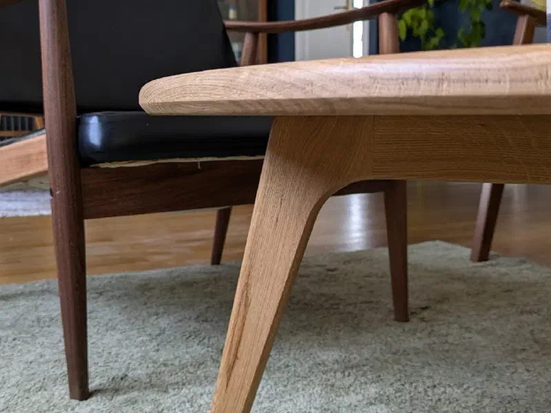 Détail d'un pied incliné de la table ronde en chêne et du chant de son plateau