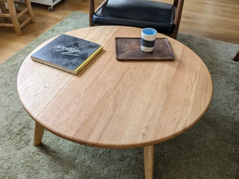 Plateau rond en chêne vu de trois quarts, un livre et un plateau en noyer posés dessus