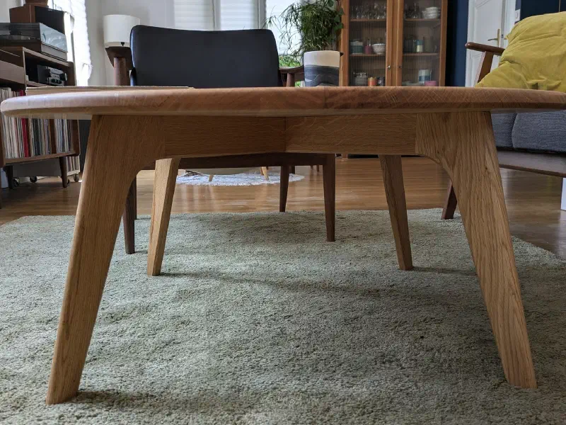 Table ronde en chêne vue au ras du sol : pieds inclinés et ceinture aux courbes douces