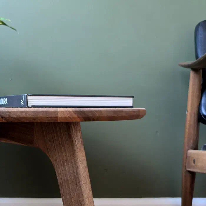 Chant adouci du plateau rond en noyer, un livre posé dessus, à côté d'un fauteuil vintage