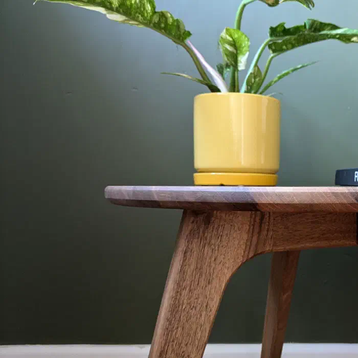 Pied incliné et ceinture courbe de la table ronde en noyer, devant un mur vert olive